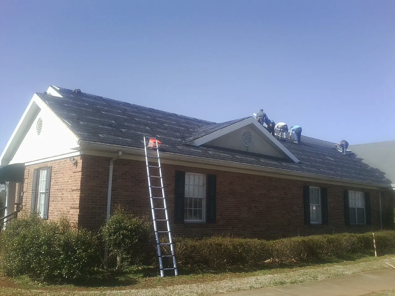 Crew tearing shingles off a brick ranch roof with a ladder set — Metal Roof Repair work by our crew in Pisgah Forest