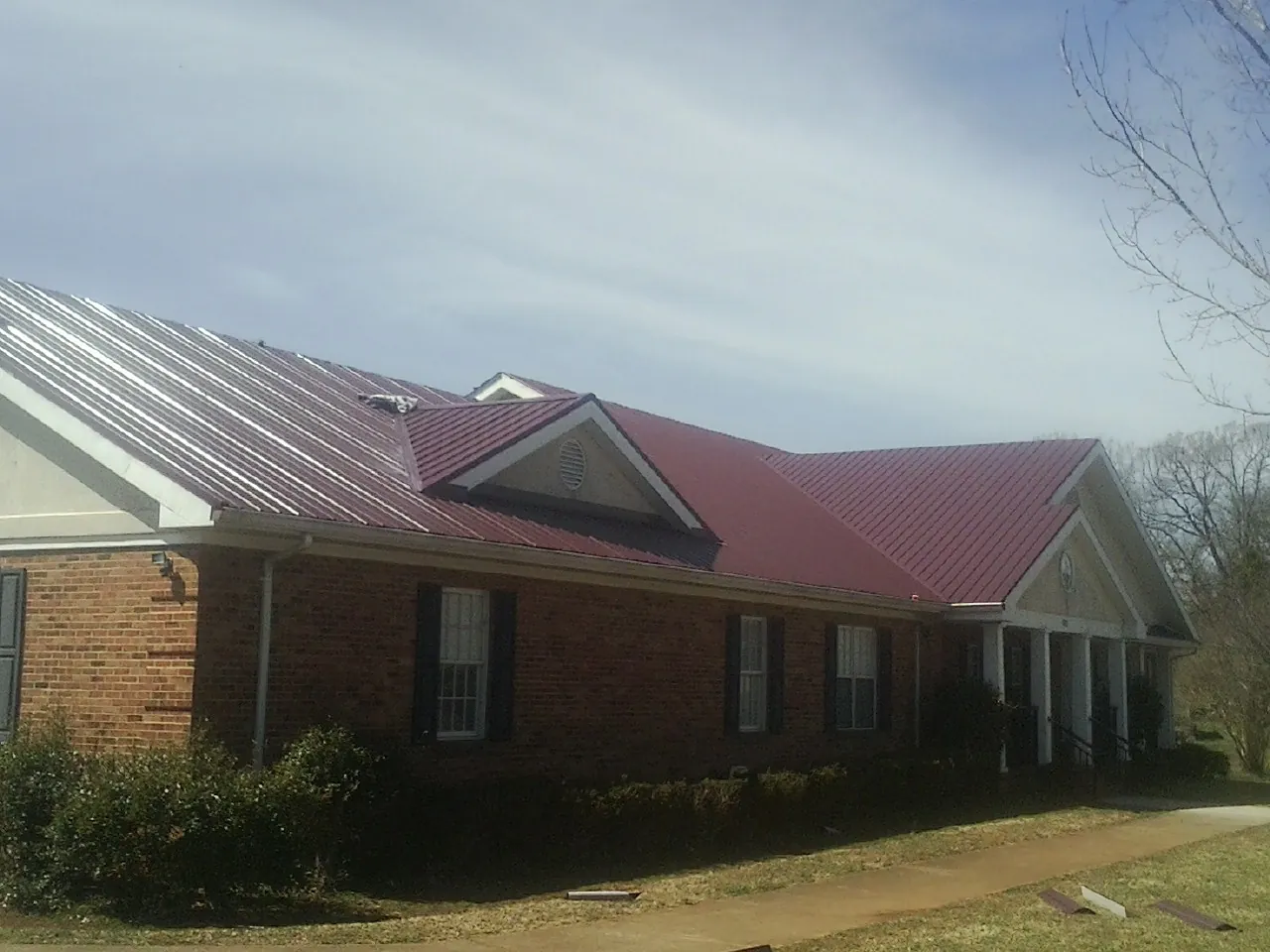 Red metal roof with gabled entries on a long brick building, from a Hail Damage Roof Repair job in Pisgah Forest
