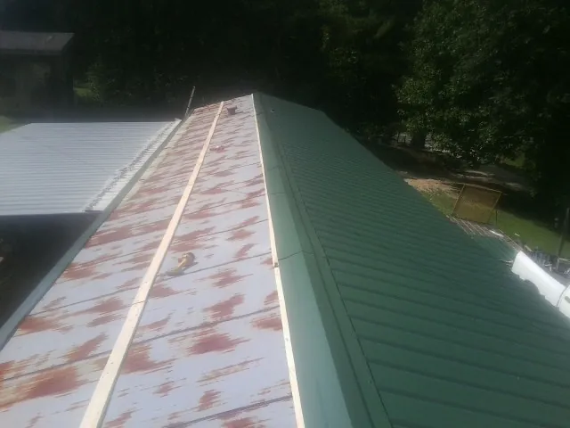 Old rusted panels beside newly installed green metal roofing — Wind Damage Roof Repair by Roofing Brothers in Pisgah Forest