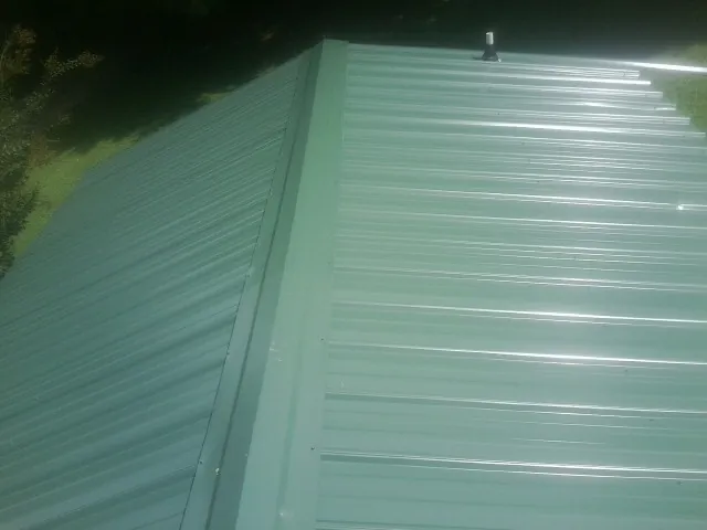 New green metal panels meeting at the ridge of a roof — Flat Roof Repair work by our crew in Pisgah Forest