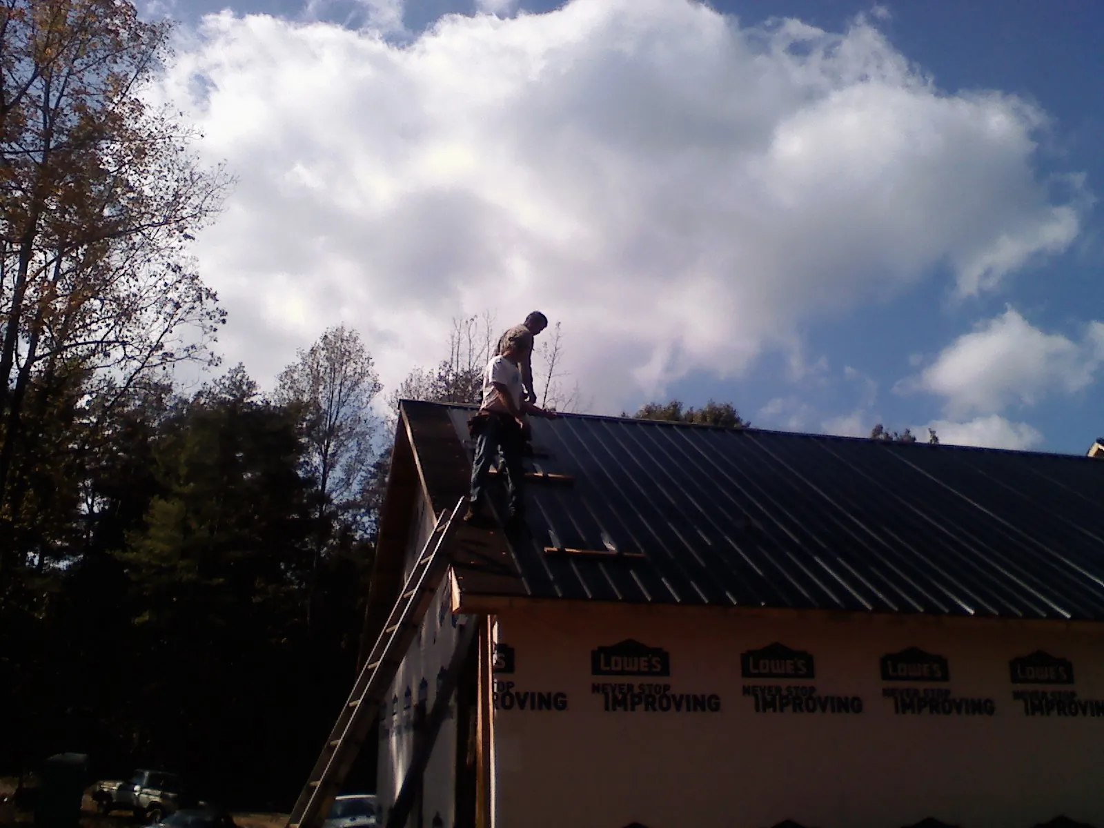 Roofer fastening dark metal panels high against a cloudy sky, from a Roof Inspection job in Pisgah Forest