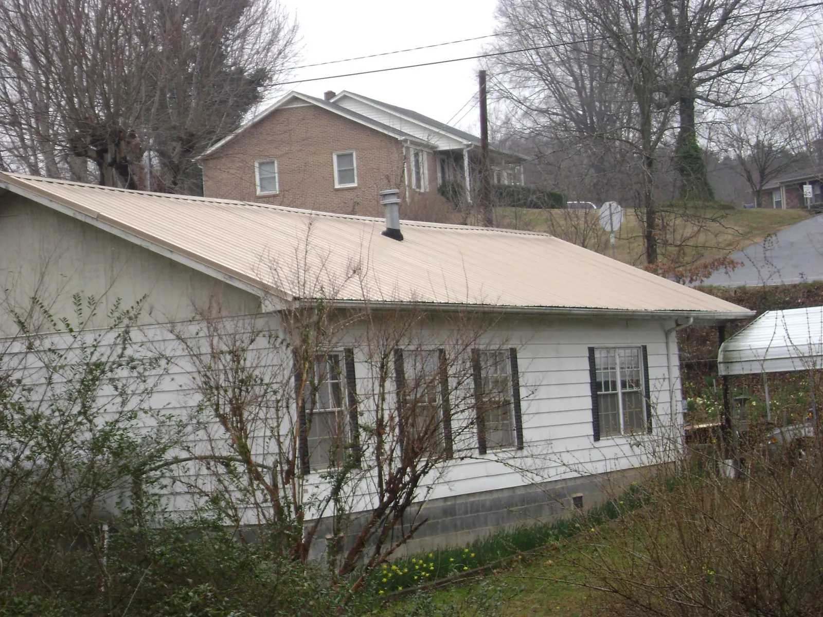 Tan metal roof on a white sided house set into a hillside — Commercial Roofing by Roofing Brothers in Pisgah Forest