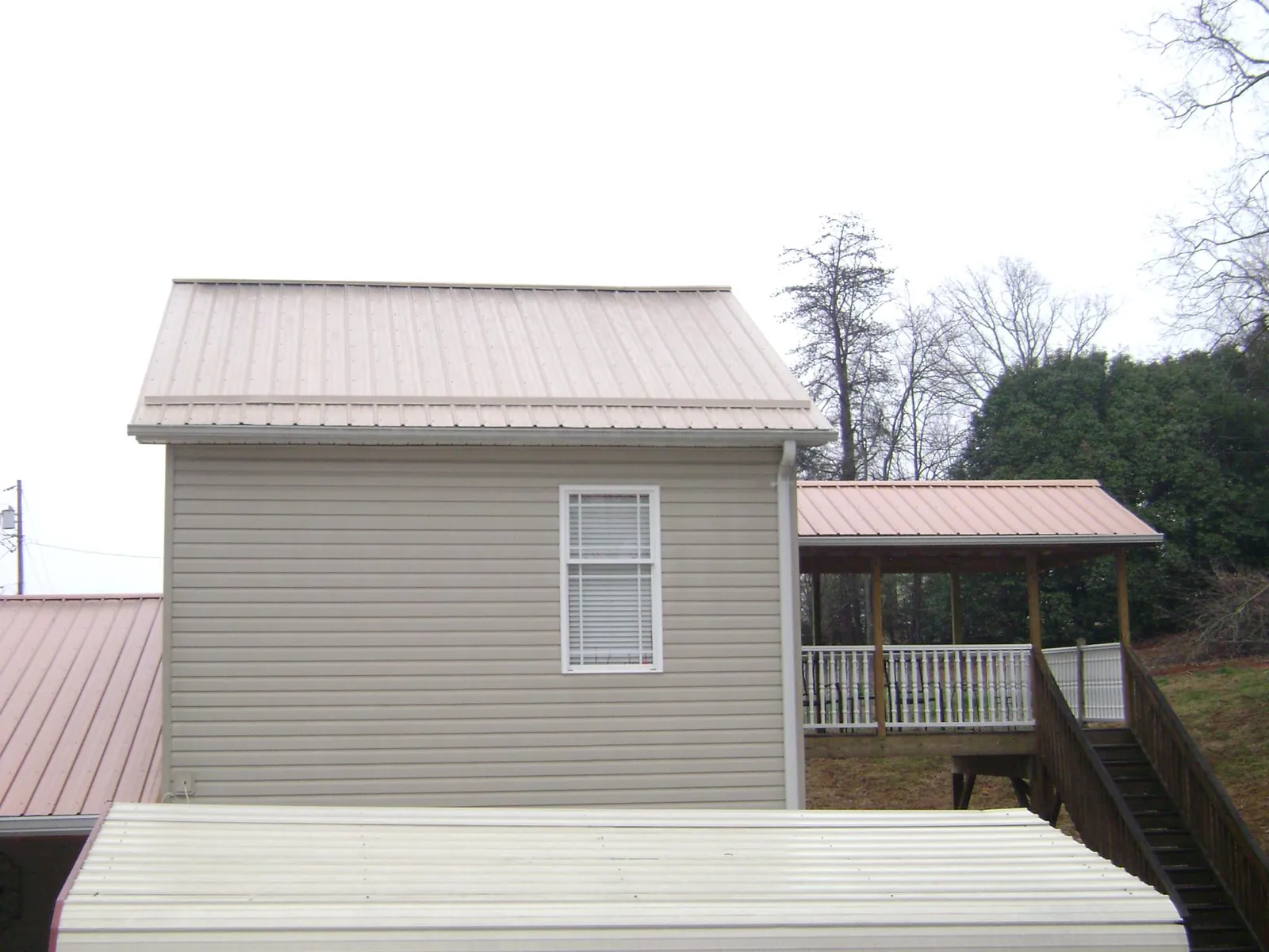 Tan metal roofs on a two story addition and attached porch, from a Roof Replacement job in Pisgah Forest